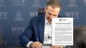Man in a blue suit signs a formal government contract document at a desk, MTY logos visible in the blurred background