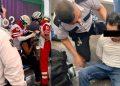 Two Emergency Responders in Red and White Uniforms Treat a Seated Person on a Stretcher; a Security Officer Watches Nearby in a Public Setting. - Apoyo Regio