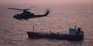 Estados Unidos Y El Conflicto De Medio Oriente - Apoyo Regio Military Helicopter Hovering Above a Tanker Ship on Calm Sea at Sunset, Pinkish Sky Reflecting on Water - Apoyo Regio