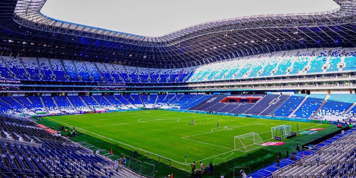Interior of a Modern Soccer Stadium with a Green Pitch and Blue Seating Surrounding an Empty Arena Under a Curved Roof. - Apoyo Regio
