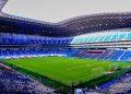 Interior of a Modern Soccer Stadium with a Green Pitch and Blue Seating Surrounding an Empty Arena Under a Curved Roof. - Apoyo Regio