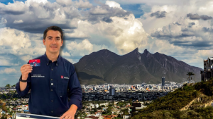 Man in a navy shirt holds up a red card in front of a cityscape with a mountain range and cloudy sky in the background.