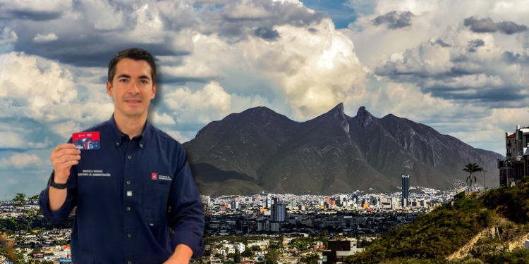 Man in a Navy Shirt Holds Up a Red Card in Front of a Cityscape with a Mountain Range and Cloudy Sky in the Background. - Apoyo Regio