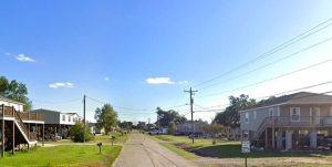 Quiet suburban street lined with raised houses on both sides and a clear blue sky ahead.