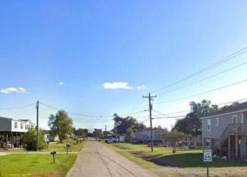 Quiet suburban street lined with raised houses on both sides and a clear blue sky ahead.