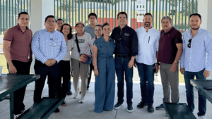 Group of eleven adults standing together outdoors, posing for a casual team photo under a pavilion.