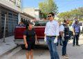 Group of Adults Standing on a Sunny Sidewalk Beside a Red Pickup Truck; a Man in a White Shirt with Gloves and Sunglasses Speaks to Others Nearby. - Apoyo Regio