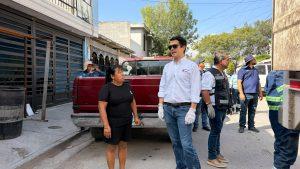 Group of adults standing on a sunny sidewalk beside a red pickup truck; a man in a white shirt with gloves and sunglasses speaks to others nearby.