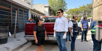 Group of Adults Standing on a Sunny Sidewalk Beside a Red Pickup Truck; a Man in a White Shirt with Gloves and Sunglasses Speaks to Others Nearby. - Apoyo Regio