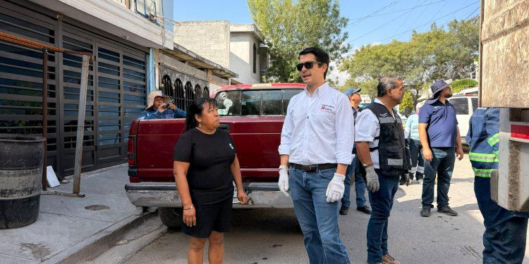 Group of Adults Standing on a Sunny Sidewalk Beside a Red Pickup Truck; a Man in a White Shirt with Gloves and Sunglasses Speaks to Others Nearby. - Apoyo Regio
