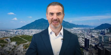 Professional Man in a Navy Suit Speaking in Front of a City Skyline with Mountains in the Background, Wearing a Clip-on Microphone. - Apoyo Regio